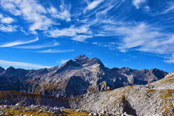 Gora Tosc odpira razgled na pogorje Triglava pod koprenastimi oblaki modrega neba. 
