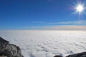 Grintovec se dviga visoko nad prostrano ravnino megle pod modrim nebom.