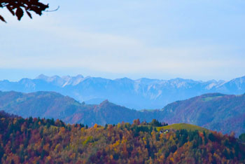 S Hleviške planine se odpira razgled na gozdnata hribovja in modre gore v ozadju.
